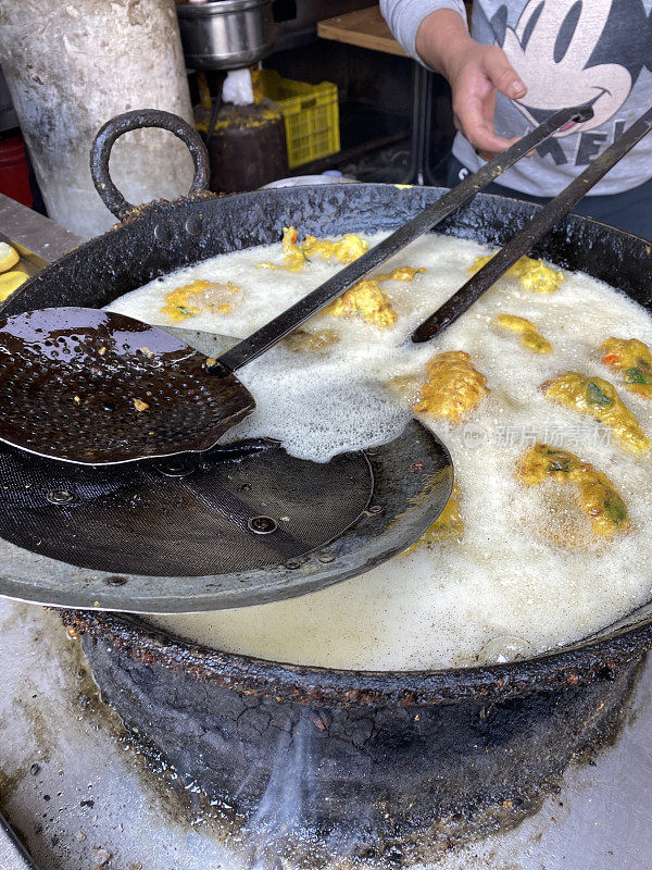 金色的Medu vada(软油条)早餐小吃，户外炉子上的街头小吃，厨师用开槽的勺子转动由Vigna mungo(黑扁豆)制成的美味甜甜圈，煎锅里的油沸腾，前景的焦点上升